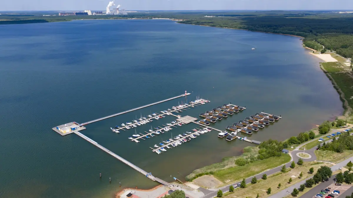 Lausitzer Seenland: 17.06.2026, Sachsen, Klitten: Boote liegen im Klittener Hafen am Bärwalder See, einem ehemaligen Tagebau, im Wasser, dahinter ist das Kohlekraftwerk Boxberg zu sehen. (Luftaufnahme mit Drohne) Foto: Robert Michael/dpa +++ dpa-Bildfunk +++