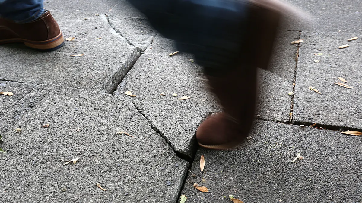 19.09.2018, Nordrhein-Westfalen, Köln: ILLUSTRATION: Ein Mann geht auf einem Bürgersteig über eine hochstehende Gehwegplatte. In Nordrhein-Westfalens Städten stürzen Fußgänger regelmäßig über Stolperfallen auf Gehwegen. (zu dpa: "Stolperfalle Gehweg - Wenn Bürger ihre Stadt verklagen") Foto: Oliver Berg/dpa +++ dpa-Bildfunk +++