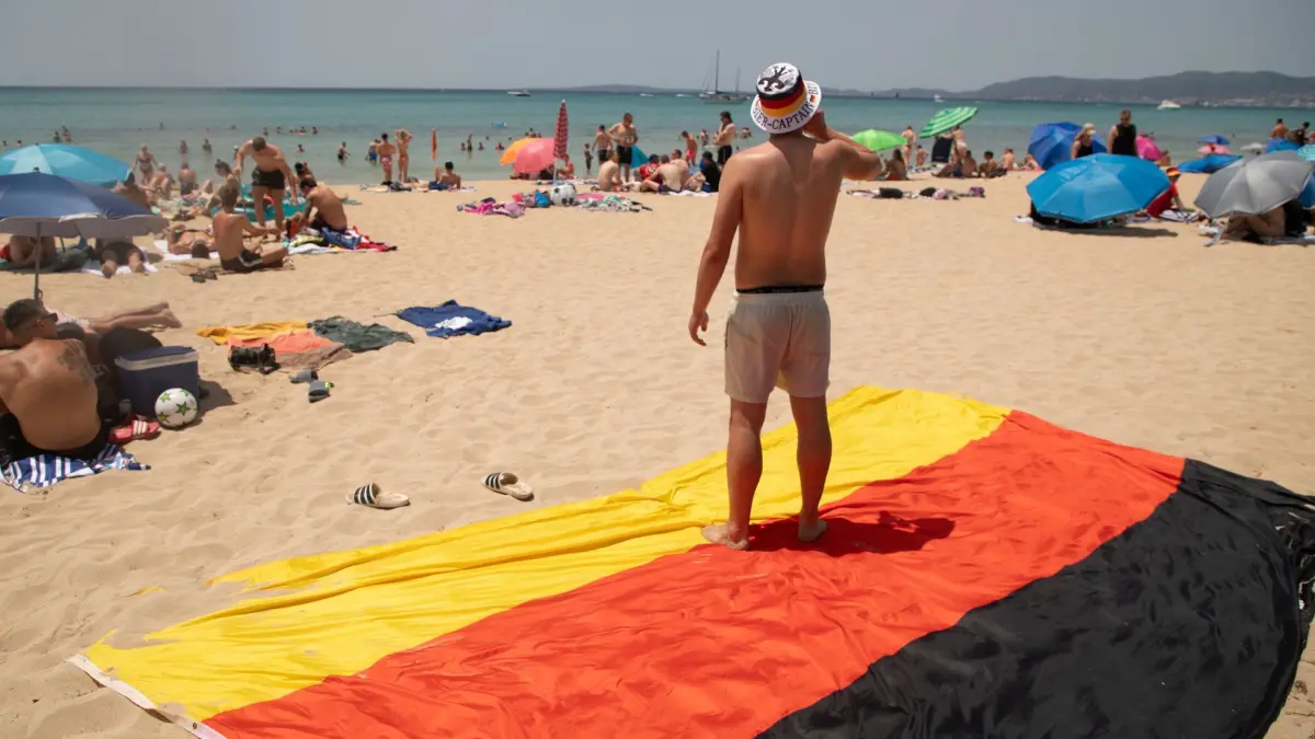 WM 2026 - Fußballfans auf Mallorca: 20.06.2026, Spanien, Palma: Fußball: vor dem Spiel Deutschland gegen die Elfenbeinküste. Ein Mann steht auf einem übergroßen Deutschlandstrandtuch am Strand „Playa de Palma“ auf Mallorca. Foto: Clara Margais/dpa +++ dpa-Bildfunk +++