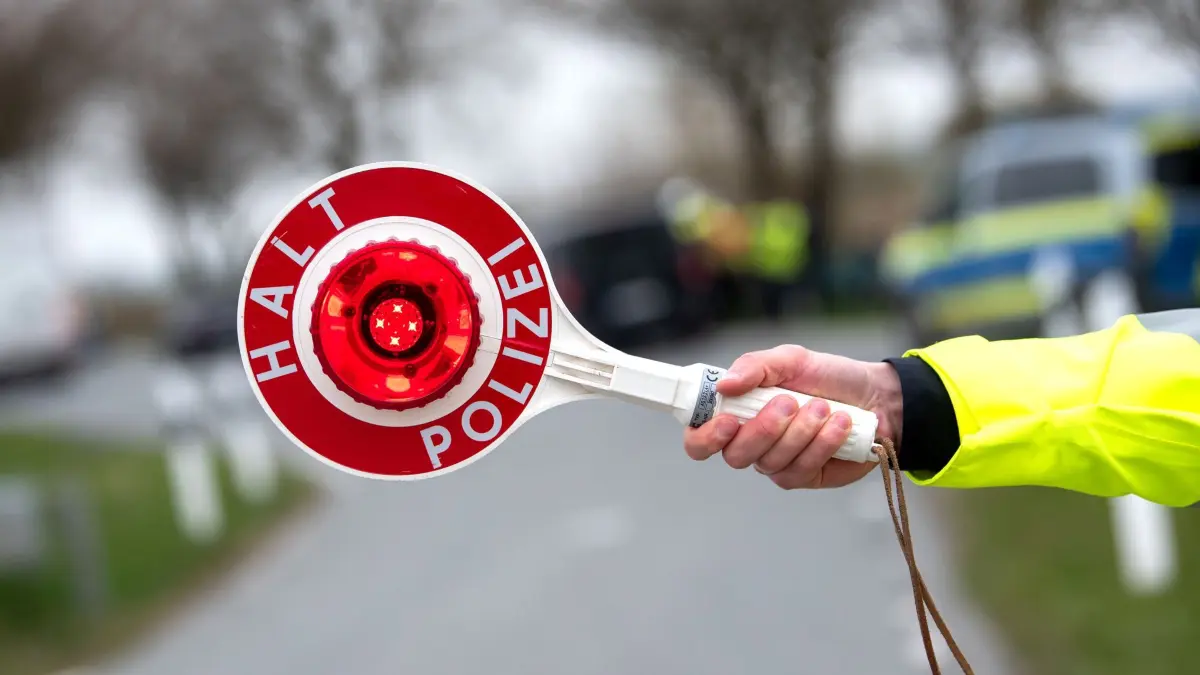 Verkehrskontrolle: ILLUSTRATION - 13.04.2026, Schleswig-Holstein, Heide: Ein Beamter hält eine "Polizeikelle" mit der Aufschrift "Halt Polizei" in die Luft. (Symbolbild) (zu dpa: «Mit 14 Menschen: Polizei stoppt völlig überladenes Auto») Foto: Daniel Bockwoldt/dpa +++ dpa-Bildfunk +++