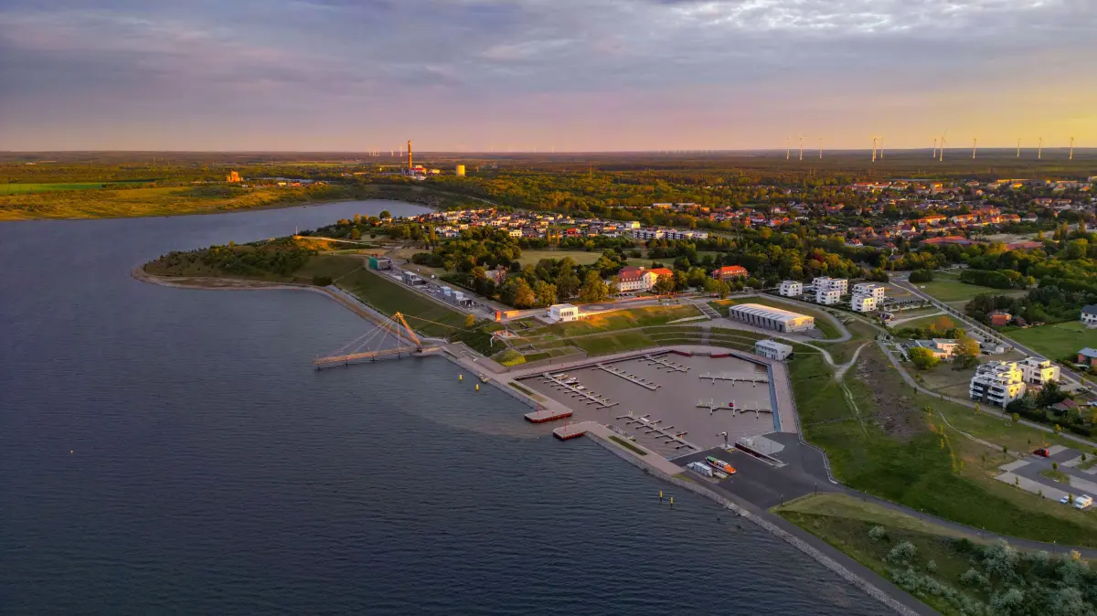 Der Großräschener See mit seinem Hafen am frühen Morgen kurz nach dem Sonnenaufgang (Luftaufnahme mit einer Drohne). Nach Auskunft der Lausitzer und Mitteldeutsche Bergbau-Verwaltungsgesellschaft mbH (LMBV) soll ab Pfingsten der Großräschener See für eine definierte Anzahl von Booten und Wasserfahrzeugen für die Saison 2024 frei gegeben werden. Der für eine Zwischennutzung notwendige Mindestwasserstand im Bergbaufolgesee wurde zum Beginn der Saison erreicht. Der Hafen Großräschen wurde bereits im Jahr 2019 eröffnet. Mit der Futung des ehemaligen Braunkohletagebaus wurde im Jahr 2007 begonnen. Für 2026 wird angestrebt, dass die Restlochkette - mit dem Sedlitzer See, dem Geierswalder See und dem Partwitzer See - zusammen mit dem Großräschener See in die dauerhafte Nutzung gehen könnte.
