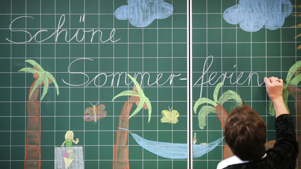 Sommerferien: SYMBOLBILD - 23.06.2015, Nordrhein-Westfalen, Dortmund: Eine Lehrerin schreibt «Schöne Sommer-ferien» an eine Tafel in einer Grundschule. (zu dpa: «Was es über Hamburgs Ferienpass zu wissen gilt») Foto: Ina Fassbender/dpa +++ dpa-Bildfunk +++
