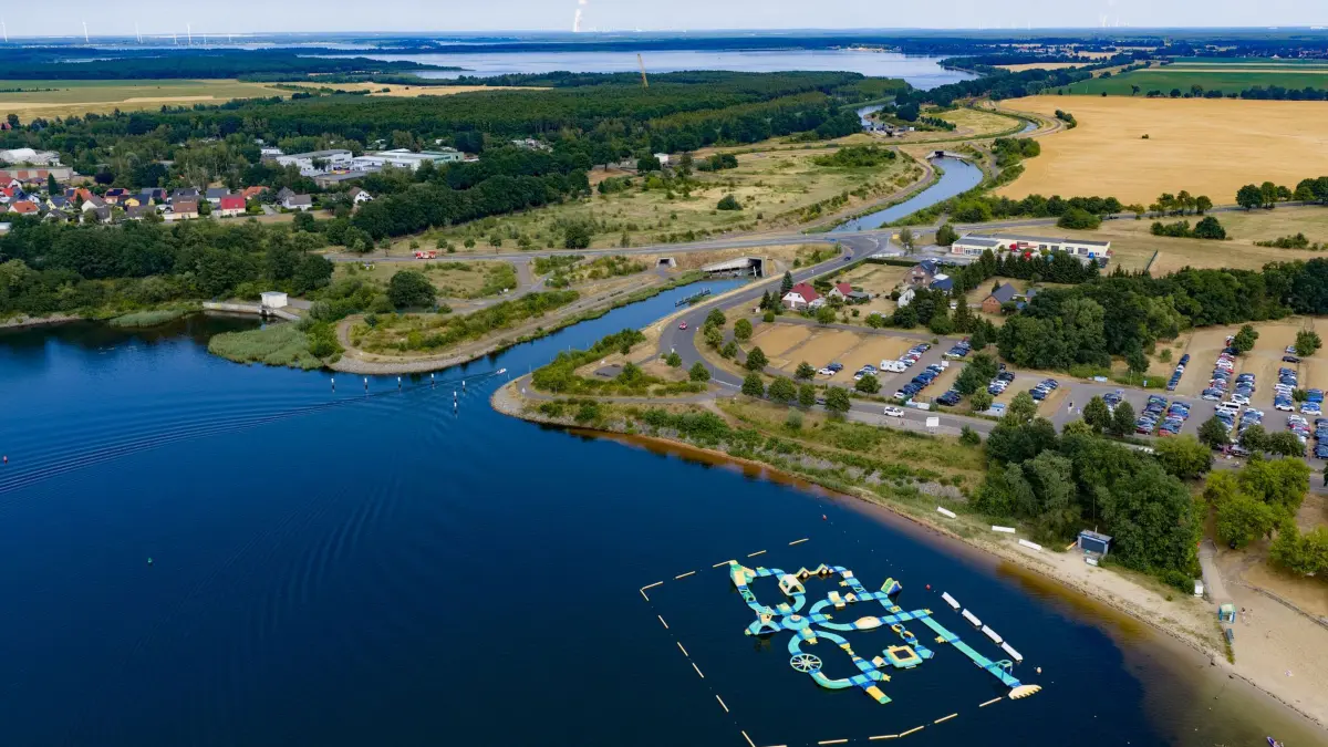 Fünf Seen in Brandenburg und Sachsen werden ein Seenland: 29.06.2026, Brandenburg, Senftenberg: Blick vom Senftenberger See in Brandenburg auf den Koschener Kanal zum Geierswalder See in Sachsen. Fünf Seen in der Lausitz werden zu einer Seenkette. Fast 60 Jahre nach der Flutung des ersten Sees verschmelzen heute Senftenberger See, Geierswalder See, Partwitzer See, Sedlitzer See und Großräschener See über schiffbare Kanäle zu einem Verbund. Sie entstanden aus gefluteten Tagebauen, der Senftenberger See war der Erste. (Luftaufnahme mit Drohne) Foto: Robert Michael/dpa +++ dpa-Bildfunk +++