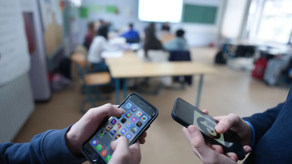Smartphones in der Schule: ILLUSTRATION - 13.02.2026, Hamburg: Zwei Schüler stehen in einem Klassenraum im Goethe-Gymnasium und schauen auf ihre Smartphones, auf einem der Displays ist das Logo der Social-Media-Plattform TikTok zu sehen. (zu dpa: «Ministerin plant Handyverbot bis Klasse 10 an Schulen») Foto: Marcus Brandt/dpa +++ dpa-Bildfunk +++