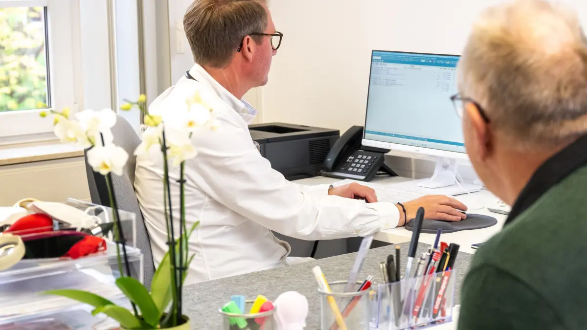 Ein Arzt schaut vor einem Patieten in einen Computer: ILLUSTRATION - Bald mehr Einblick für den Betriebsarzt? Ein Referentenentwurf sieht vor, dass Betriebsärzte künftig auf die elektronische Patientenakte zugreifen können – Beschäftigte müssten aktiv widersprechen. (zu dpa: «E-Akte für Betriebsärzte: Patienten können Zugang sperren») Foto: Benjamin Nolte/dpa-tmn - Honorarfrei nur für Bezieher des dpa-Themendienstes +++ dpa-Themendienst +++