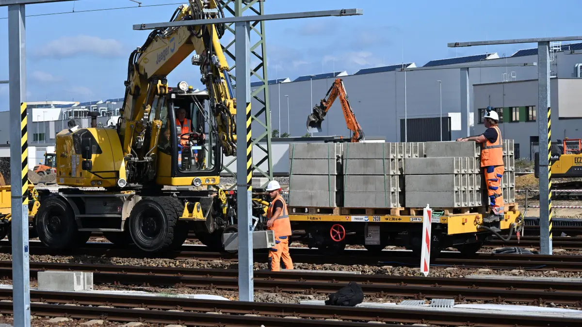 DB Hubschrauber Strommast: Luftballett am neuen Cottbuser Bahnwerk
In Cottbus laufen die Bauarbeiten für die Fertigstellung des neuen Bahnwerkes auf Hochtouren. Nicht nur am Boden, wo eine zweite riesige Halle für die Instandhaltung von ICE-Zügen entsteht, ist am Freitag auch in der Luft gearbeitet worden. Ein Hubschrauber wurde eingesetzt, um die Bauarbeiten auf dem Werksgelände schneller voranzutreiben. Ein Helikopter der Schweizer Firma Heliswiss installierte insgesamt 29 Oberleitungsmasten im nördlichen Bahnhofsbereich und flog diese durch die Luft ein. Die Masten werden die neu verlegten Gleise überspannen, damit künftig ICE Züge, die ins neue Bahnwerk einfahren, mit Strom versorgt werden können.
Bereits im Januar 2026 hatte die Deutsche Bahn einen Lastenhelikopter von Heliswiss für ähnliche Bauarbeiten beauftragt. Trotz des schwierigen Winterwetters waren damals fast so viele Oberleistungsmasten durch die Luft geschwebt wie jetzt im Sommer. Dabei handelt es sich um einen Hochpräzisionsvorgang. Die tonnenschweren Masten werden exakt an die Stellen gebracht, an denen sie arretiert werden müssen. Am Boden übernehmen Monteure die Feinarbeit um die Masten auf den vorbereiteten Fundamenten zu fixieren.