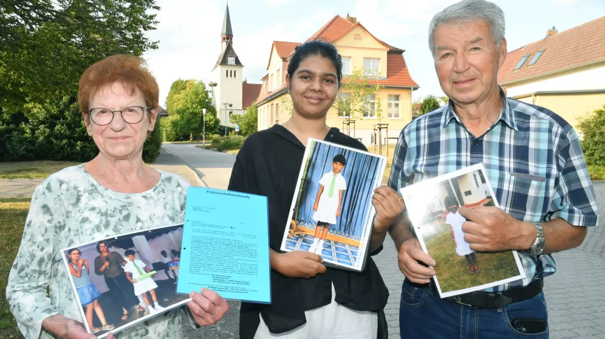 Mädchen aus Sri Lanka feiert bei erstem Auslandsaufenthalt ihres Lebens Geburtstag in Hohenleipisch: Mädchen aus Sri Lanka feiert bei erstem Auslandsaufenthalt ihres Lebens Geburtstag in Hohenleipisch
- - V.l. Doris Bormann (80), Maduki Madumini (24/25) und Jürgen Bormann (80) mit den Bildern und Unterlagen von 2009 vor der Skyline von Hohenleipisch mit Kirche, alter Schule/Bürgerhaus und Storchennest