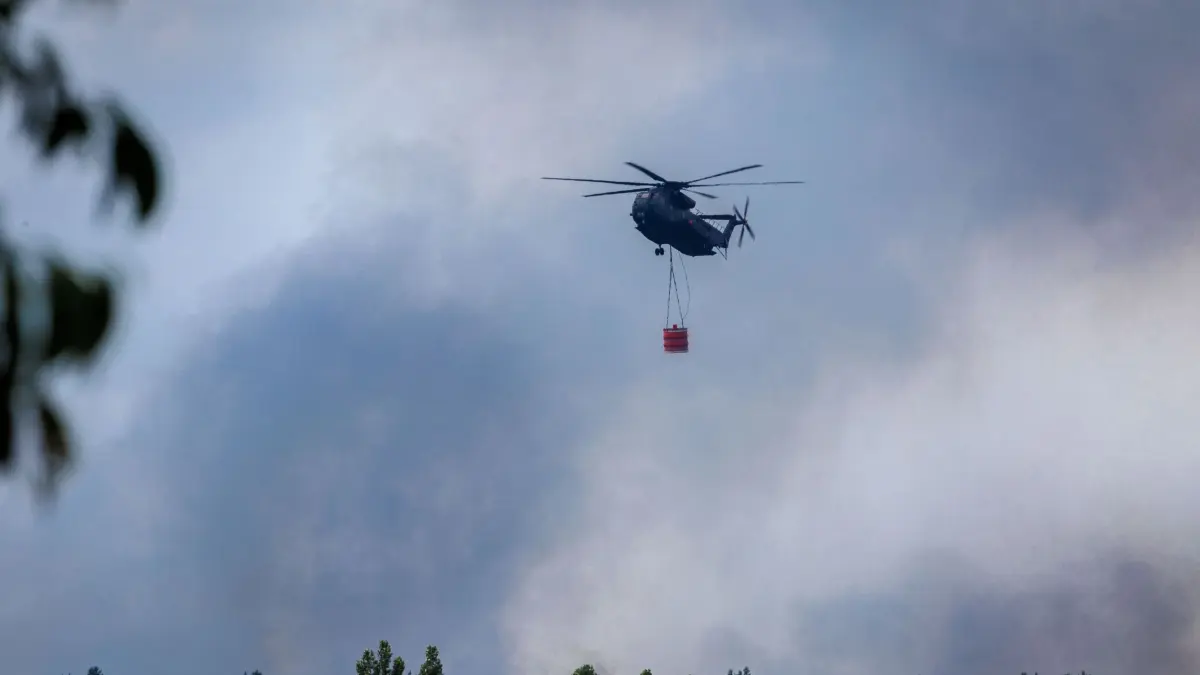 Waldbrand im Müritz-Nationalpark: 16.07.2026, Mecklenburg-Vorpommern, Kratzeburg: Ein Bundeswehr-Hubschrauber CH-53 mit einem 5000-Liter-Tank Löschwasser fliegt über dem Waldbrand im Müritz-Nationalpark. Der Großbrand auf einem ehemaligen Truppenübungsgelände hat sich auf mittlerweile 269 Hektar ausgedehnt. Derzeit sind etwa 375 Einsatzkräfte vor Ort. Foto: Jens Büttner/dpa +++ dpa-Bildfunk +++