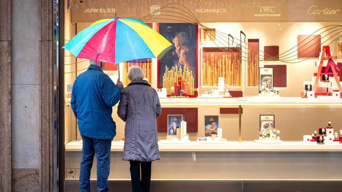 Senioren: ARCHIV - 02.12.2025, Bremen: Zwei ältere Personen stehen bei Regen vor einem Schaufenster eines Schmuckgeschäfts und betrachten die ausgestellten Waren. Sie teilen sich einen bunten Regenschirm. (zu dpa: «Gut jeder zweite Beschäftigte über 50 will früher in Rente») Foto: Sina Schuldt/dpa +++ dpa-Bildfunk +++