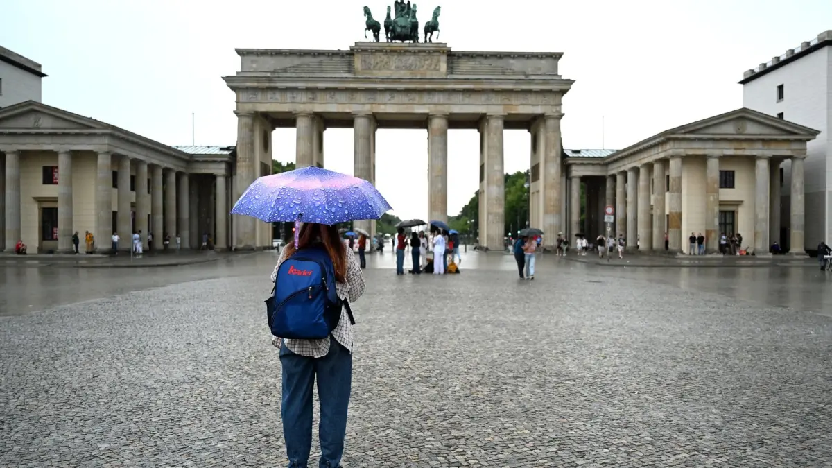 Wetter in Berlin: ARCHIV - 17.07.2026, Berlin: Eine Frau steht mit Regenschirm vor dem Brandenburger Tor während Regen über Berlin zieht. (zu dpa: «Nur kurzer Sonnenschein - dann folgen Schauer») Foto: Elisa Schu/dpa +++ dpa-Bildfunk +++