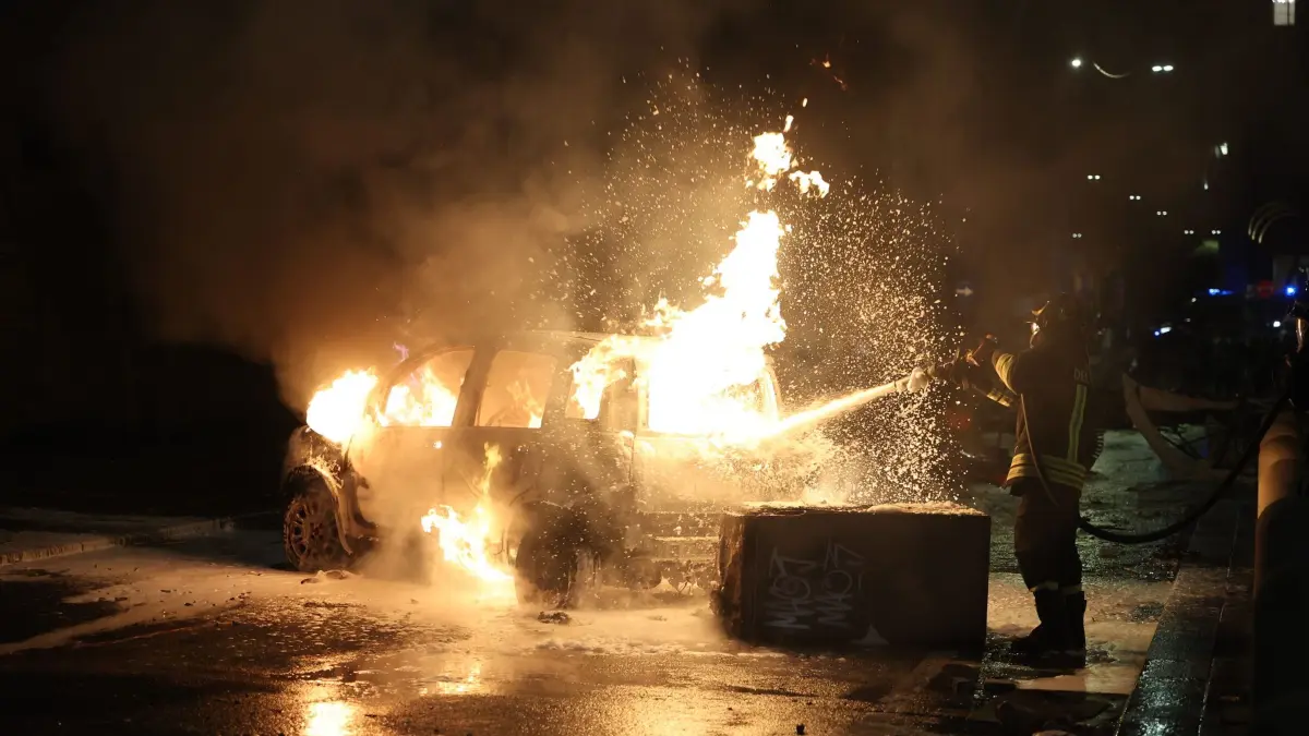 Zusammenstöße nach tödlichem Polizeieinsatz in Bologna: 21.07.2026, Italien, Bologna: Einsatzkräfte der Feuerwehr löschen ein brennendes Auto nach Auseinandersetzungen zwischen Aktivisten und Sicherheitskräften bei Protesten nach einer Gedenkkundgebung in der Innenstadt. Nach dem Tod eines Einwanderers aus Marokko bei einem gewaltsamen Einsatz der italienischen Polizei ist es in mehreren Städten zu Protesten gekommen. Foto: Guido Calamosca/LaPresse via ZUMA Press/dpa +++ dpa-Bildfunk +++