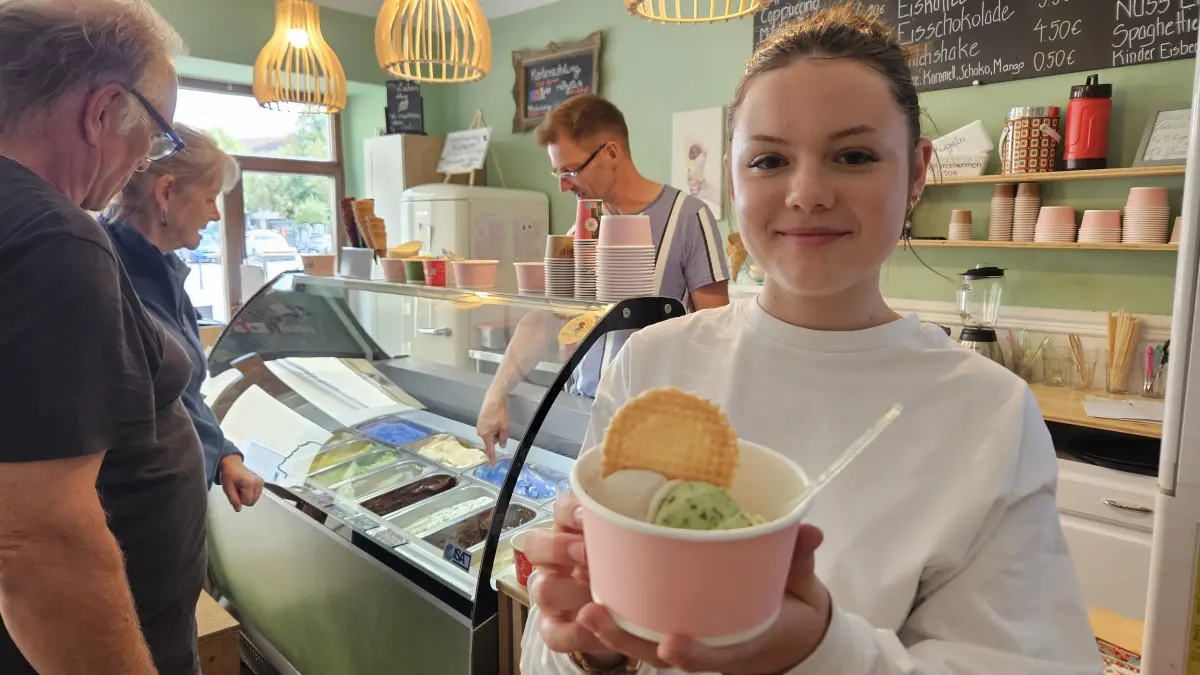 Ferienjobberin Lotta Menzel (15) präsentiert einen Eisbecher mit den neuen Trends Gurke-Melisse-Limette und Quark-Leinölcreme. Im Hintergrund berät Robert Gbureck, Inhaber der Eisdiele "Schoko & Luise" in Hoyerswerda, seine Kunden.