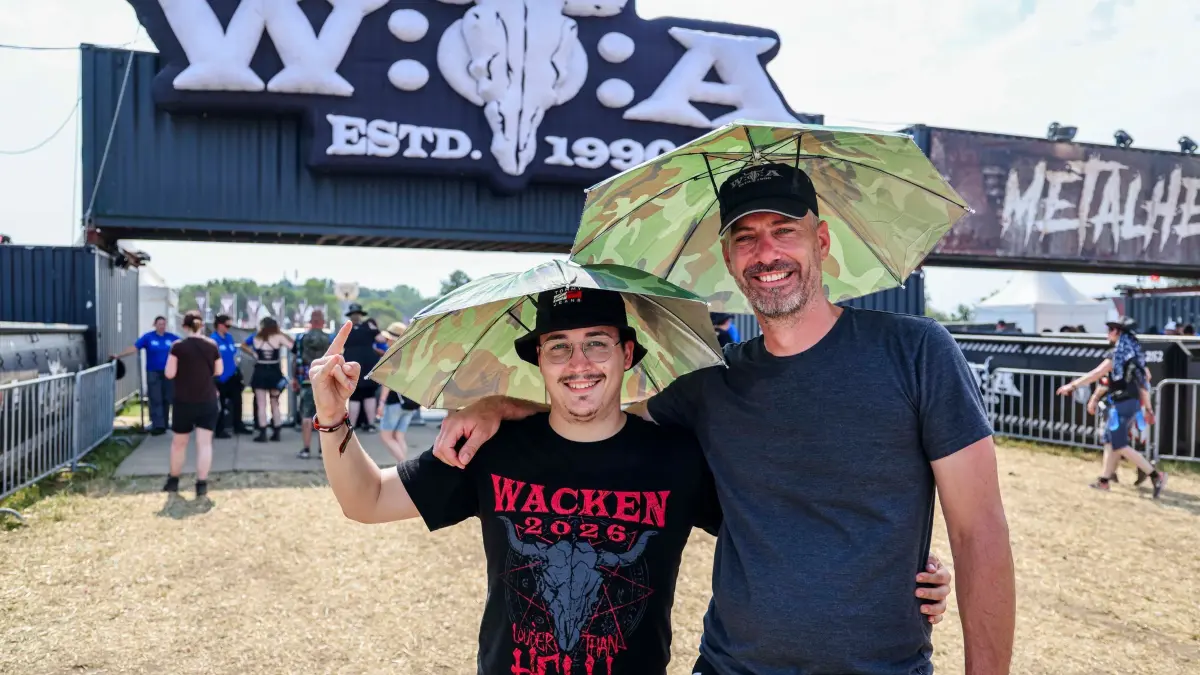 Wacken Open Air: 30.07.2026, Schleswig-Holstein, Wacken: Justin (l) und Michael trotzen der Hitze mit Sonnenschirmen beim Wacken Open Air (W:O:A). Das W:O:A gilt als größtes Heavy-Metal-Festival der Welt. Foto: Frank Molter/dpa +++ dpa-Bildfunk +++