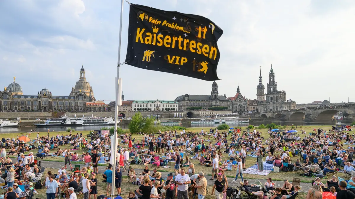 „Kaisermania 2026“ in Dresden: 31.07.2026, Sachsen, Dresden: Sogenannte Zaungäste sitzen auf den Elbwiesen gegenüber der historischen Altstadtkulisse vor Beginn des Auftaktkonzerts der "Kaisermania 2026" bei den Filmnächten am Elbufer. Am 1. und 7. August sowie am 8. August 2026 tritt Schlagersänger Roland Kaiser in Dresden wie jedes Jahr zur Show "Kaisermania" vor jeweils 12.000 Zuschauern auf. Foto: Robert Michael/dpa +++ dpa-Bildfunk +++
