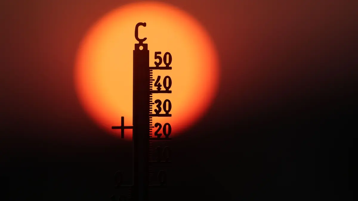 Hinter einem Thermometer geht am Morgen die Sonne auf. (zu dpa: «RKI: Rund 9.600 Tote allein durch extrem heiße Juni-Woche»)