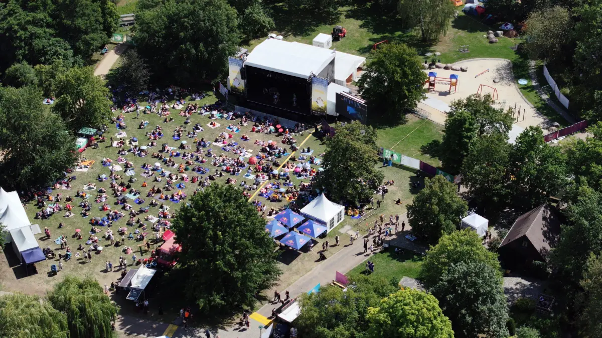 Elbenwald FestivaL 2026: Blick aus der Vogelperspektive auf das Festivalgelände und die Zeltstadt im Spreeauenpark
Elbenwald Festival im Spreeauenpark.
Der Spreeauenpark in Cottbus verwandelt sich am Wochenende wieder in eine Fantasiewelt mit Fantasy, Musik, Cosplay, Gaming und zahlreichen Mitmachangeboten. Bereits am Donnerstag und Freitag reisten viele Camper aus ganz Deutschland zum diesjährigen Elbenwald Festival an, dass offiziell am Freitag startete und bis Sonntag läuft.
Musikalisch gehören dArtagnan, Fiddler’s Green, Corvus Corax, Punk Rock Factory und Liedfett zu den bekannten Namen, die an drei Tagen im Spreeauenpark auftreten. Den traditionellen Abschluss übernimmt das Pilsen Philharmonic Orchestra mit epischer Musik aus Fantasy, Gaming und Kino. Dazu kommen Cosplay Wettbewerbe, Lesungen, Shows, Workshops, Schwertkampf, Bogenschießen, historische Tänze, Gaming, Tabletop, Rollenspiel, Karaoke, Bogenshießen und zahlreiche weitere Angebote zum Mitmachen. Auch regionale Beteiligte wie My Wife and the Microwave, der Dice Club Cottbus und die Ompah Kunstreitshow stehen im Programm.