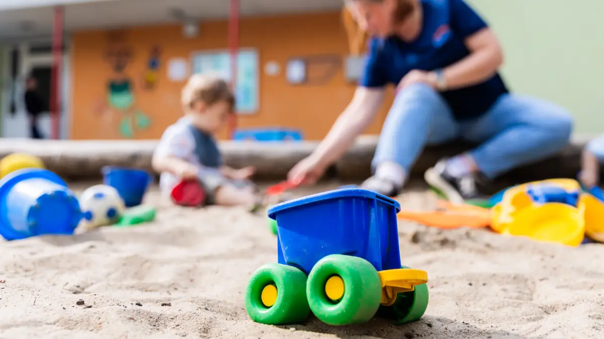 Ein Kind spielt mit einer Erzieherin im Sandkasten einer Kita. Die hochumstrittenen Lockerungen der Personalvorgaben in nordrhein-westfälischen Kitas können ab sofort umgesetzt werden. (zu dpa: «Umstrittene Kita-Personalverordnung in Kraft») +++ dpa-Bildfunk +++