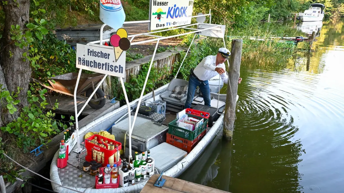 Wasserkiosk auf Rheinsberger Seenkette: ARCHIV - 13.08.2026, Brandenburg, Kleinzerlang: Als schwimmender Lieferservice ist Wasserkiosk-Betreiber Jens Winkelmann auf seinem dafür umgebauten Kahn unterwegs. Er versorgt Urlauber auf Hausbooten, Jachten und Paddelbooten mit Eis, hausgebackenem Kuchen, kalten Getränken und geräuchertem Fisch. Er verkehrt auf der Rheinsberger Seenkette. (zu dpa: «Schwimmender Kiosk biegt auf die Zielgerade für dieses Jahr») Foto: Jens Kalaene/dpa +++ dpa-Bildfunk +++