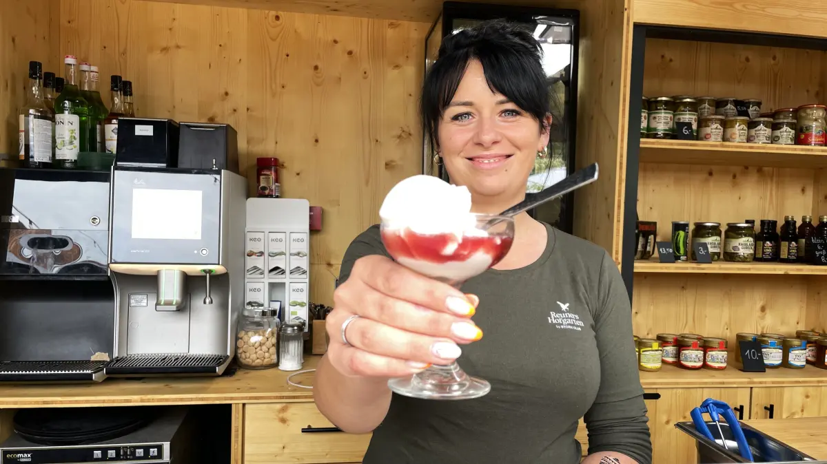 Denise Reuner hält am 28.08.2026 eine Kugel Whiskey-Sour-Eis mit Rotwein in Reuners Hofgarten in Schlepzig in die Kamera.