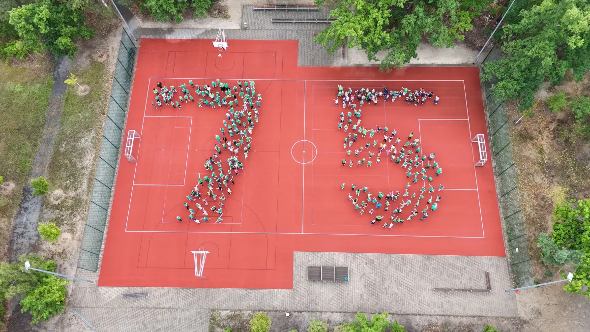 Auf dem Sportplatz der Berggrundschule bilden anlässlich eines Geburtstages die Schüler eine 75.