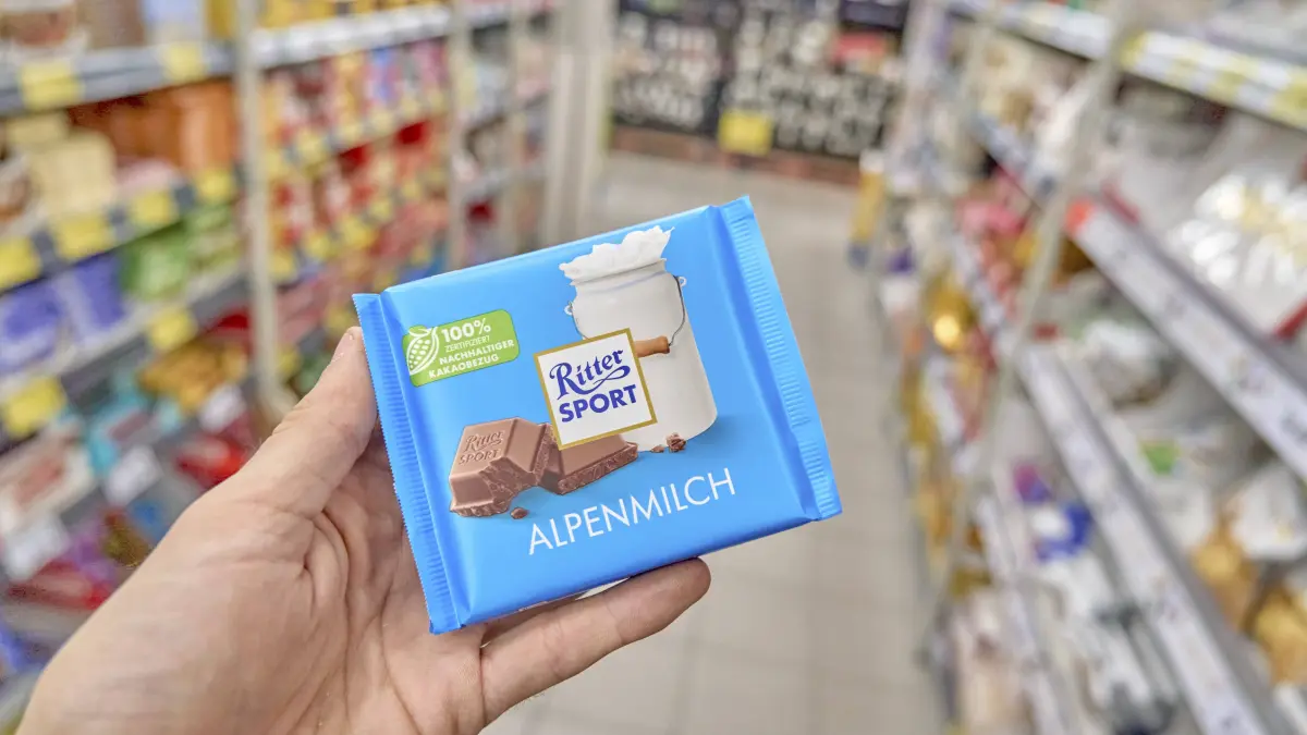 Hand hält eine blaue Ritter Sport Alpenmilch Tafel vor einem Supermarktregal, Süßigkeit, Schokolade, Kaufland, Supermarkt, Deutschland Hand holding a blue Ritter Sport Alpenmilch bar in front of a supermarket shelf, candy, chocolate, Kaufland, supermarket, Germany Copyright: imageBROKER/brandxnews iblbee18316964.jpg Bitte beachten Sie die gesetzlichen Bestimmungen des deutschen Urheberrechtes hinsichtlich der Namensnennung des Fotografen im direkten Umfeld der Veröffentlichung