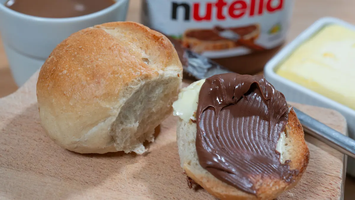 Ein Brötchen mit Nutella liegt auf einem Frühstücksbrett.