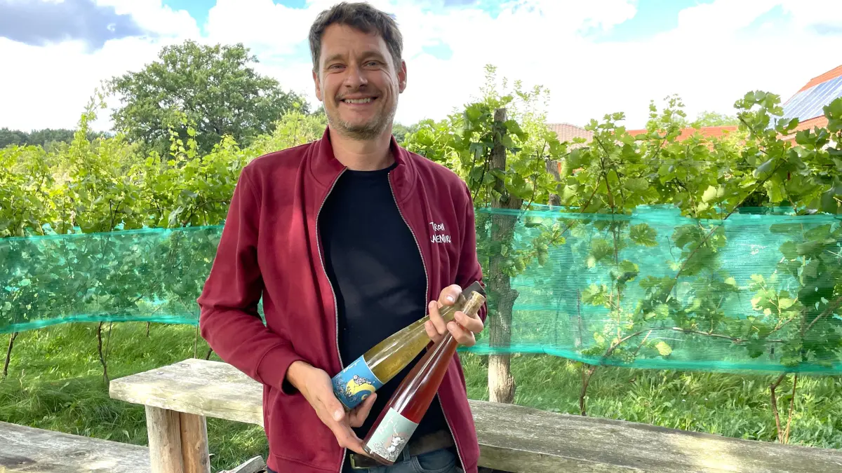 Winzer Gernot Kleinlein mit zwei seiner Weine vor Rebstöcken auf seinem Grundstück in Dobbrikow im Teltow-Fläming am 31.08.2026