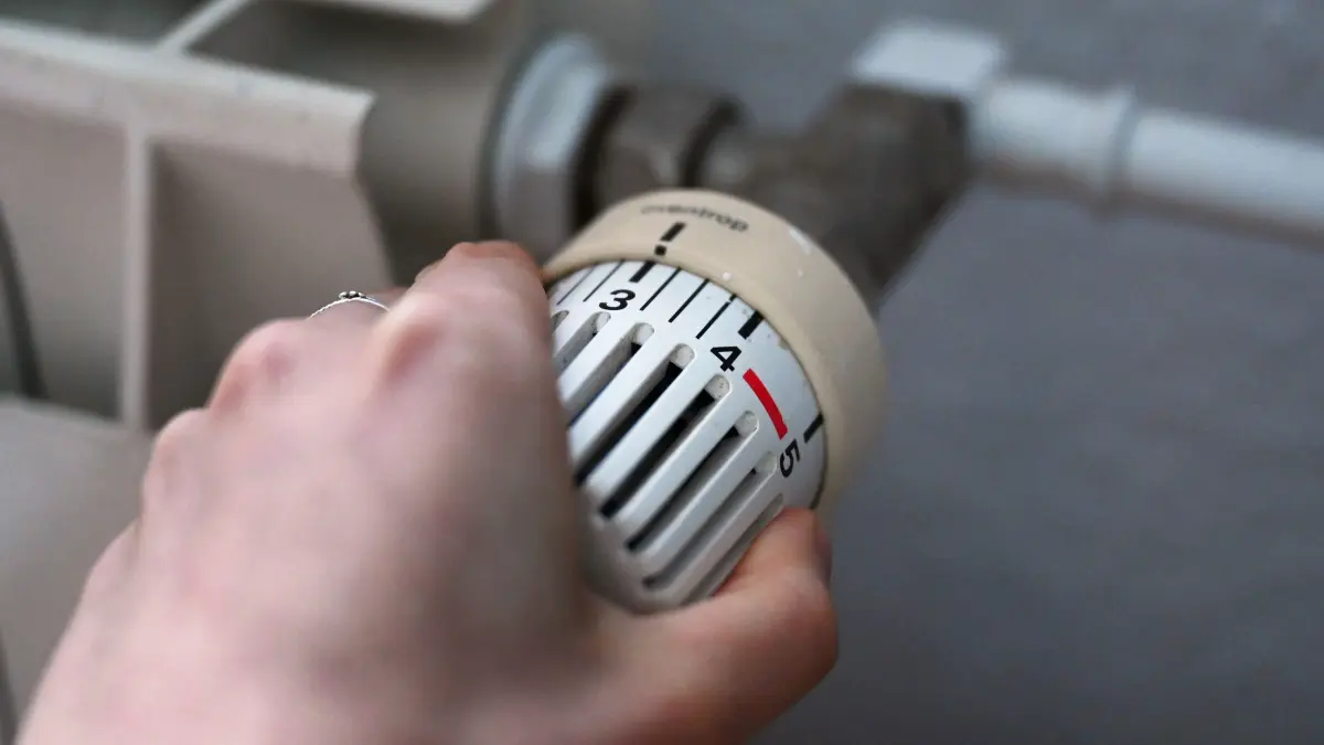 Eine Frau dreht an einem Thermostatregler einer Heizung in einer Wohnung.