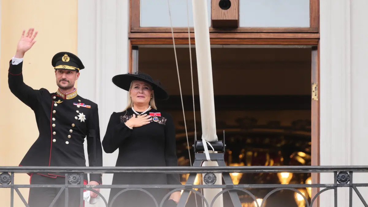 Auf dem Balkon des Königlichen Schlosses zeigt sich das neue Königspaar den Menschen in Oslo: Während König Haakon VIII. der Menge zuwinkt, legt Königin Mette-Marit sichtlich bewegt die Hand auf ihr Herz.
