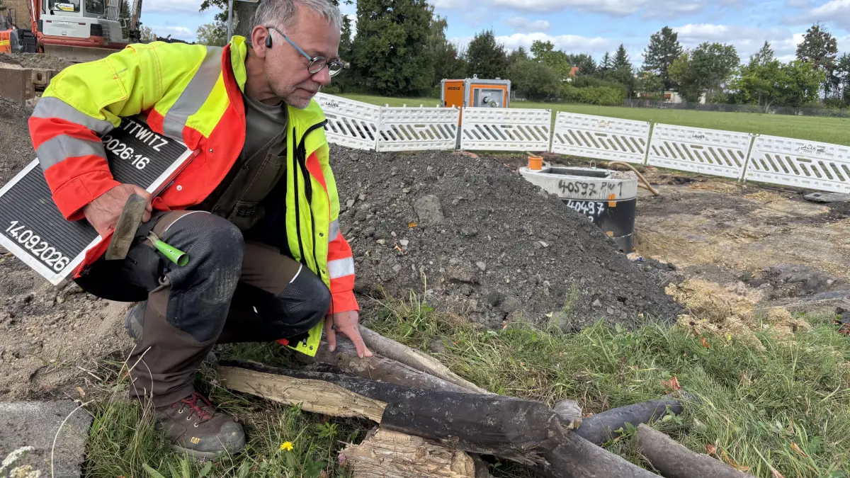 Archäologe Jens Lipsdorf zeigt Überreste eines freigelegten historischen Fahrweges. Wie lange die Stämme im Boden gelegen haben, ist noch ungewiss.