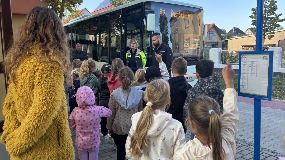 Busfahrer André Theile erklärt Erstklässlern an der Haltestelle Verkehrs- und Benimmregeln. Neben ihm stehen Polizistin Susan Gölsdorf (links) und NVG‑Geschäftsführer Mario Vogel (ganz links). Gerade an Haltestellen im Landkreis kommt es immer wieder zu Situationen, in denen diese Regeln fehlen.