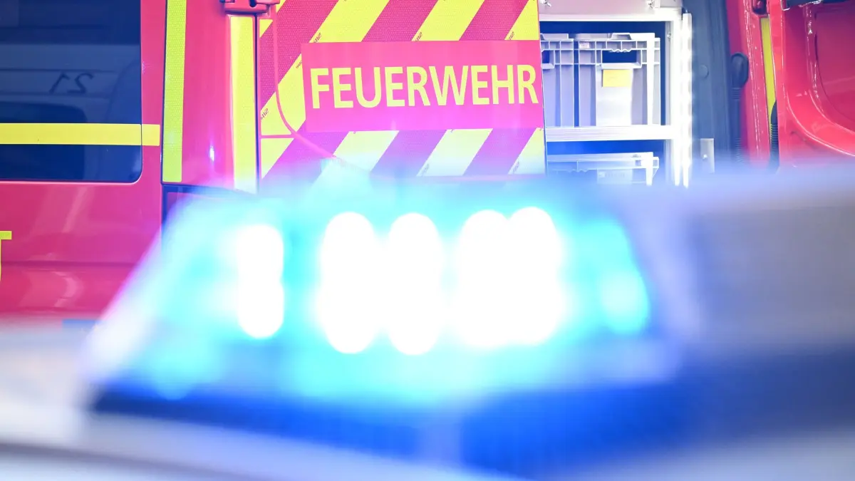 Feuerwehr Symbolbild: Ein Fahrzeug der Feuerwehr steht bei einem Einsatz auf einer Straße, während im Vordergrund das Blaulicht eines Polizeifahrzeugs zu sehen ist. (zu dpa: «Flugzeug kollidiert am Flughafen mit Feuerwehrfahrzeug»)