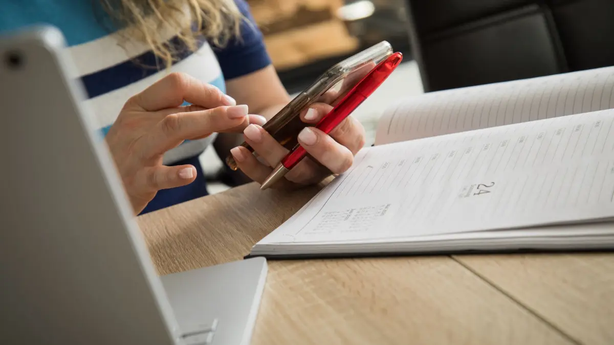 Eine Frau mit Handy, Laptop und Kalender: ILLUSTRATION - Urlaubstage-Tetris kann sich lohnen: Wer seine Tage geschickt nutzt, hat länger am Stück frei. (zu dpa: «Brückentage 2027 und Urlaub: Holen Sie das Maximum heraus») Foto: Christin Klose/dpa-tmn - Honorarfrei nur für Bezieher des dpa-Themendienstes +++ dpa-Themendienst +++