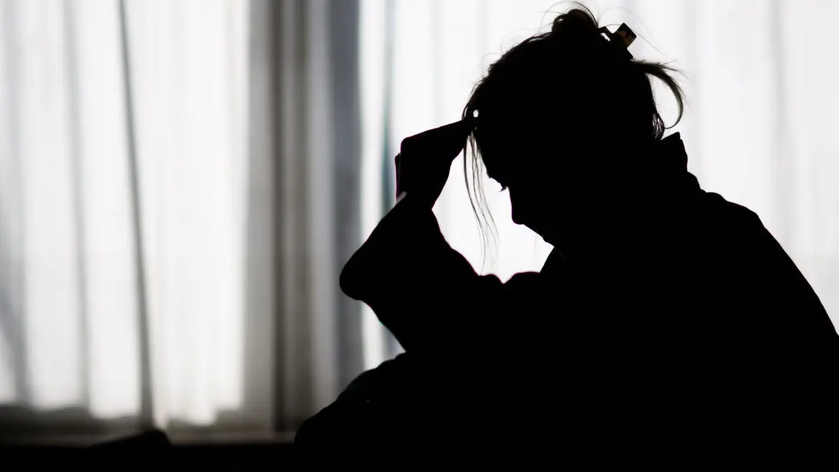 Depression: ILLUSTRATION - Die Silhouette einer Frau zeichnet sich vor einer hellen Fensterfront ab (gestellte Szene). (zu dpa: «AOK: Psychische Leiden treiben Krankentage in die Höhe»)