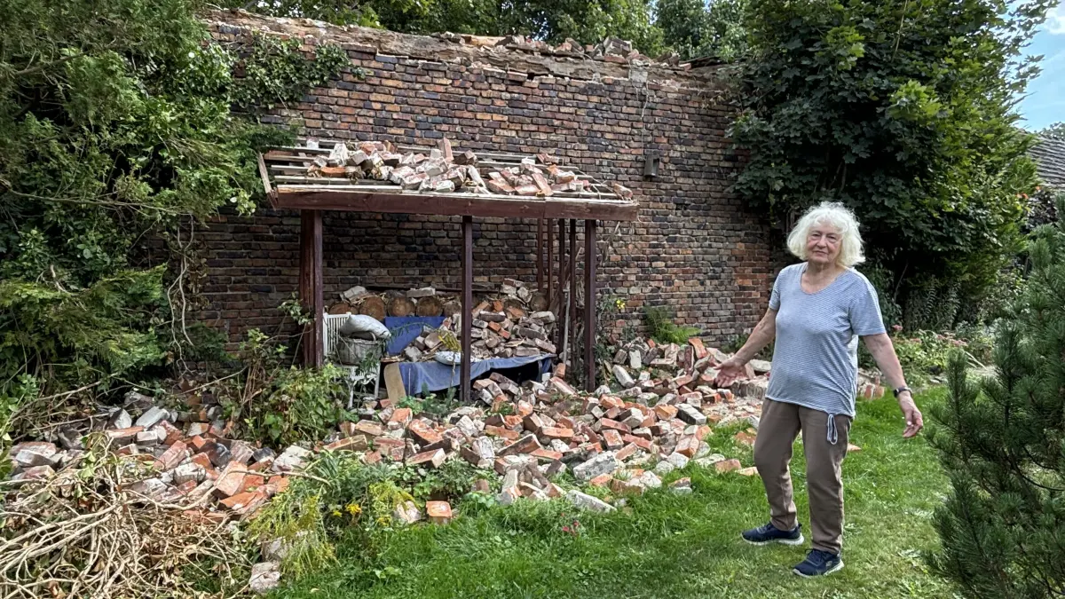 Marie Anne Laurence Delesalle-Günzel aus Podrosche vor den Aufräumarbeiten des halb eingestürzten benachbarten Gebäudes, dessen halber Giebel sich über ihren Garten und den kleinen Teich ergoss. Die Steine kommen weg, doch was wird mit dem entstandenen Schaden auf ihrem Grundstück?