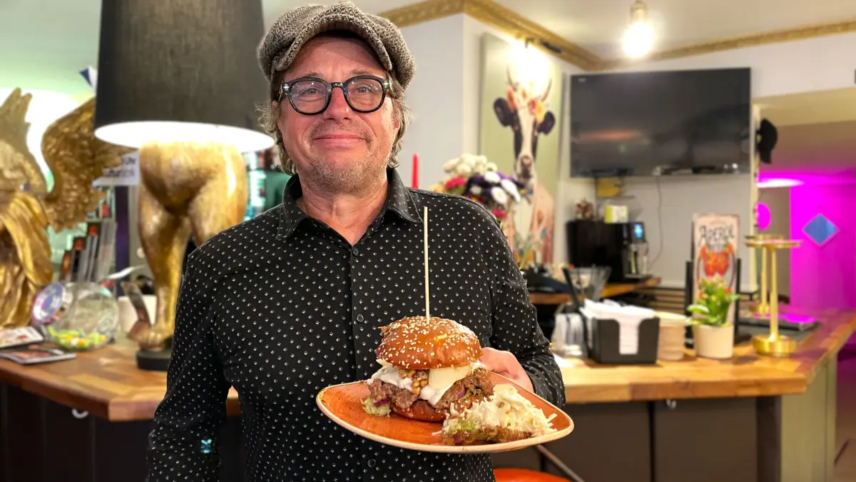 Stefan Ziehm alias Hanny hält einen Burger mit Ziegenkäse und Walnüssen in Hanny's Restaurant in Fürstenwalde in die Kamera am 07.20.2026.
