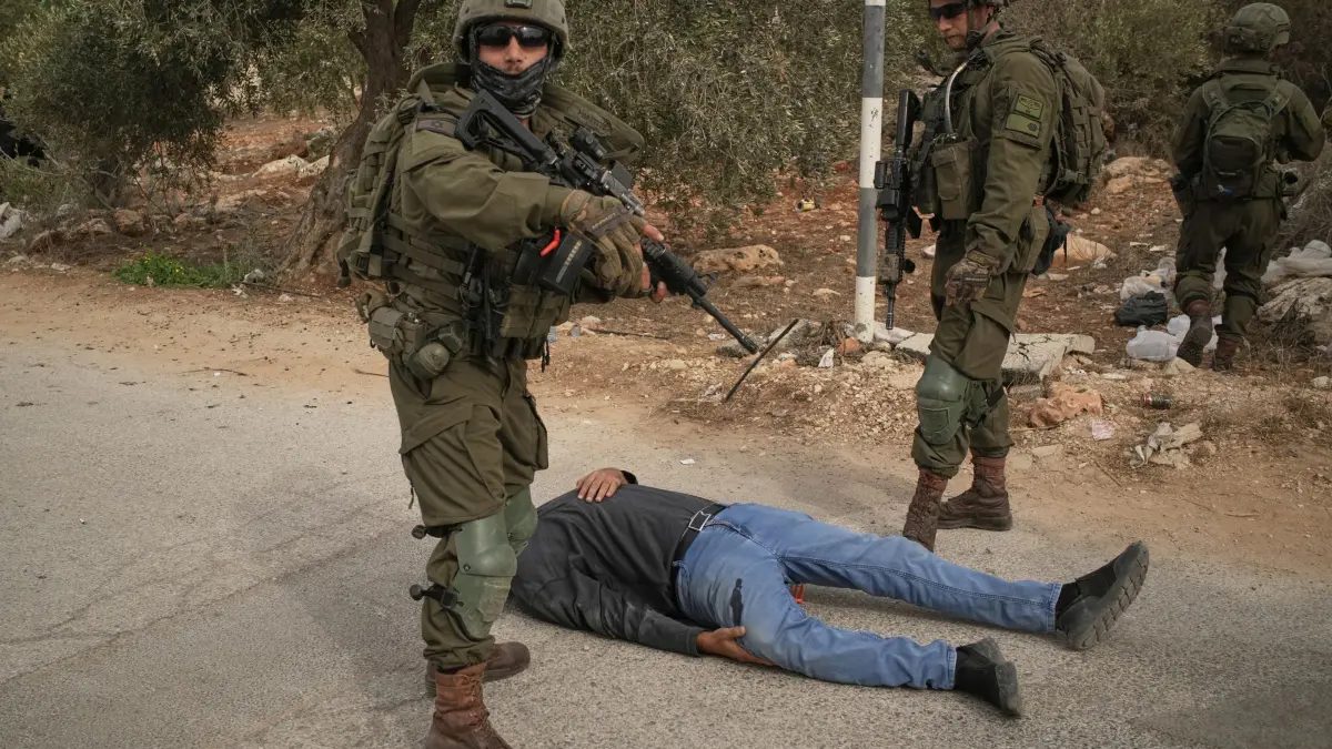 Nahostkonflikt - Abu Falah: 16.10.2026, Palästinensische Gebiete, Abu Falah: Israelische Soldaten stehen neben einem verwundeten Palästinenser, der auf einer Straße liegt, nachdem sie ihn angeschossen hatten. Dies geschah nach einem Angriff von Siedlern auf Palästinenser, die im Dorf Abu Falah im Westjordanland Oliven pflückten. Foto: Leo Correa/AP/dpa +++ dpa-Bildfunk +++