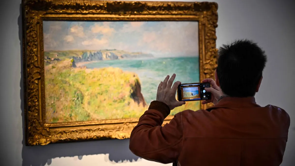 FRANCE-CULTURE-ART-AUCTION: A man takes a picture of the painting 'Bord des falaises à Pourville' by French painter Claude Monet displayed as part of The Durand-Ruel Collection 'Generations of Vision' before being auctioned at the Christie's auction house in Paris on October 16, 2026. The auction will take place on October 22, 2026. (Photo by JULIEN DE ROSA / AFP) / RESTRICTED TO EDITORIAL USE