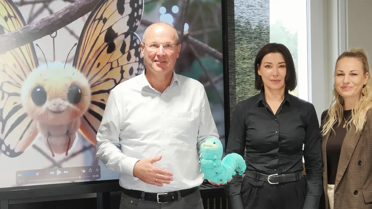 Steffen Markgraft, Geschäftsführer der Wohnungsgesellschaft Hoyerswerda präsentiert die kleine Raupe gemeinsam mit der Geschäftsführerin von my:uniquate, Carol Wiesner sowie Hobart von der Wohnungsgesellschaft vor einem Standbild des Imagefilms.