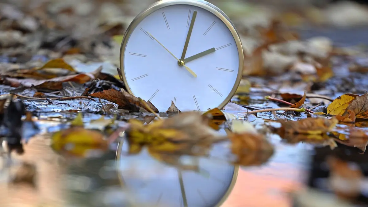 Zeitumstellung: Eine Uhr spiegelt sich im blätterbedeckten Wasser. Mit Beginn der Winterzeit werden in Deutschland und den meisten anderen Ländern Europas am Sonntagmorgen (26. Oktober) die Uhren von 3.00 Uhr auf 2.00 Uhr zurückgestellt. Bis zum 29. März 2026 gilt dann wieder die mitteleuropäische Zeit (MEZ), auch Winterzeit genannt. (zu dpa: «Uhren zurückgestellt - Winterzeit hat begonnen»)
