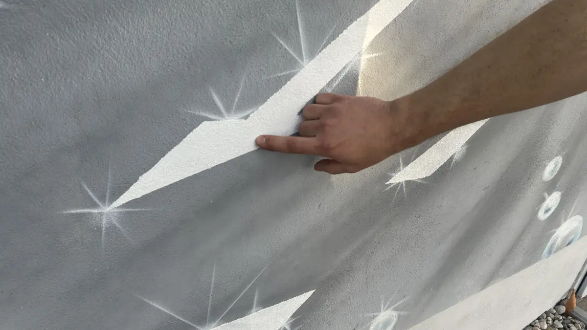 Tobias Gmerek, Produktionsleiter bei Swarco in Schönborn, weist auf die Glasperlen hin, die weltweit zum Einsatz kommen. Im Graffiti sind sie als Teil der Straßenmarkierung direkt ins Motiv integriert.